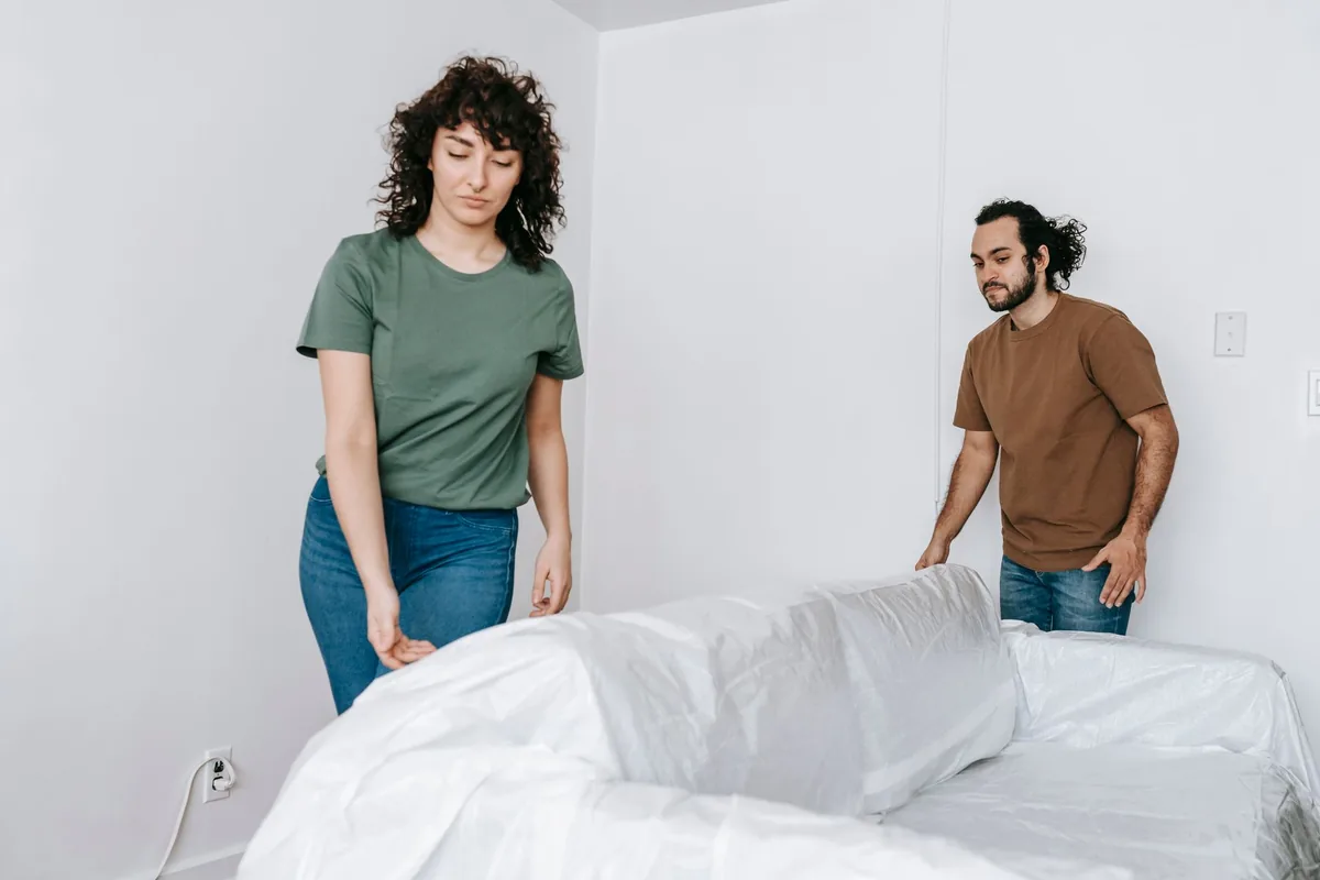 Zwei Personen schützen ein Sofa mit einer Transporthülle