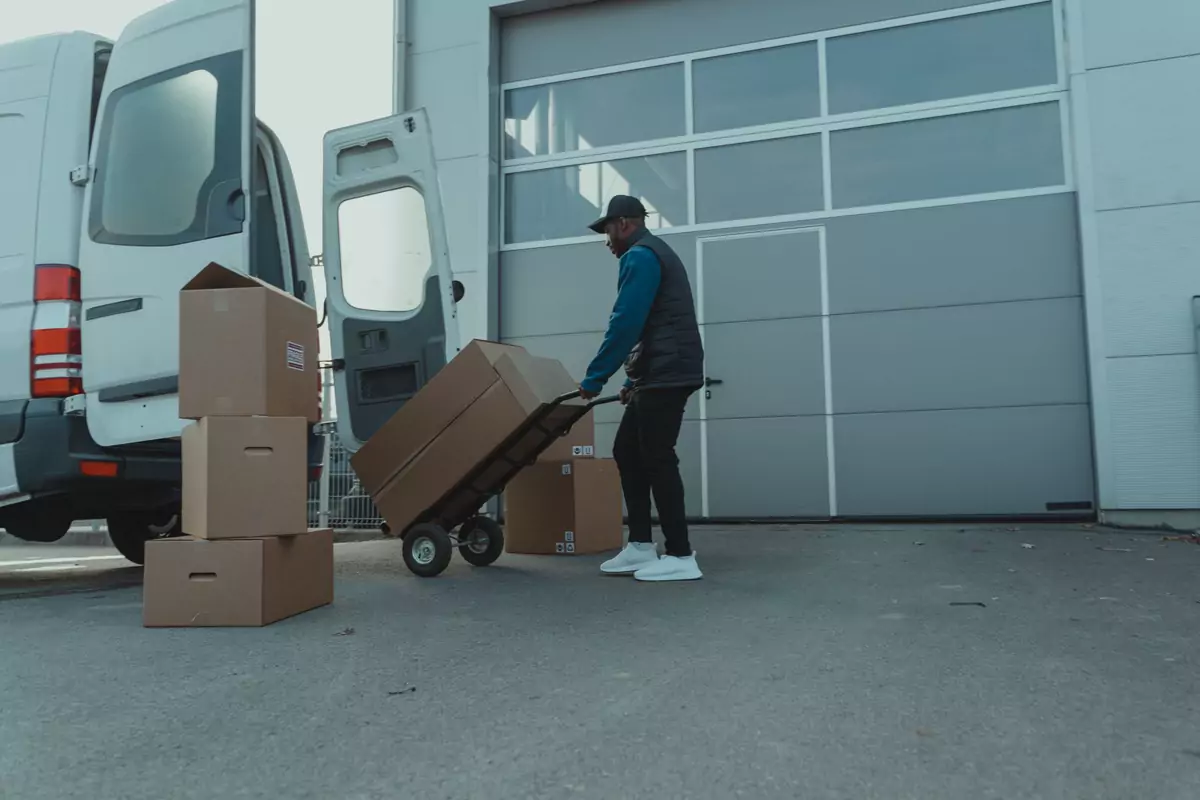 Ein Transportmitarbeiter zieht gestapelte Kartons mit einer Sackkarre zum Fahrzeug